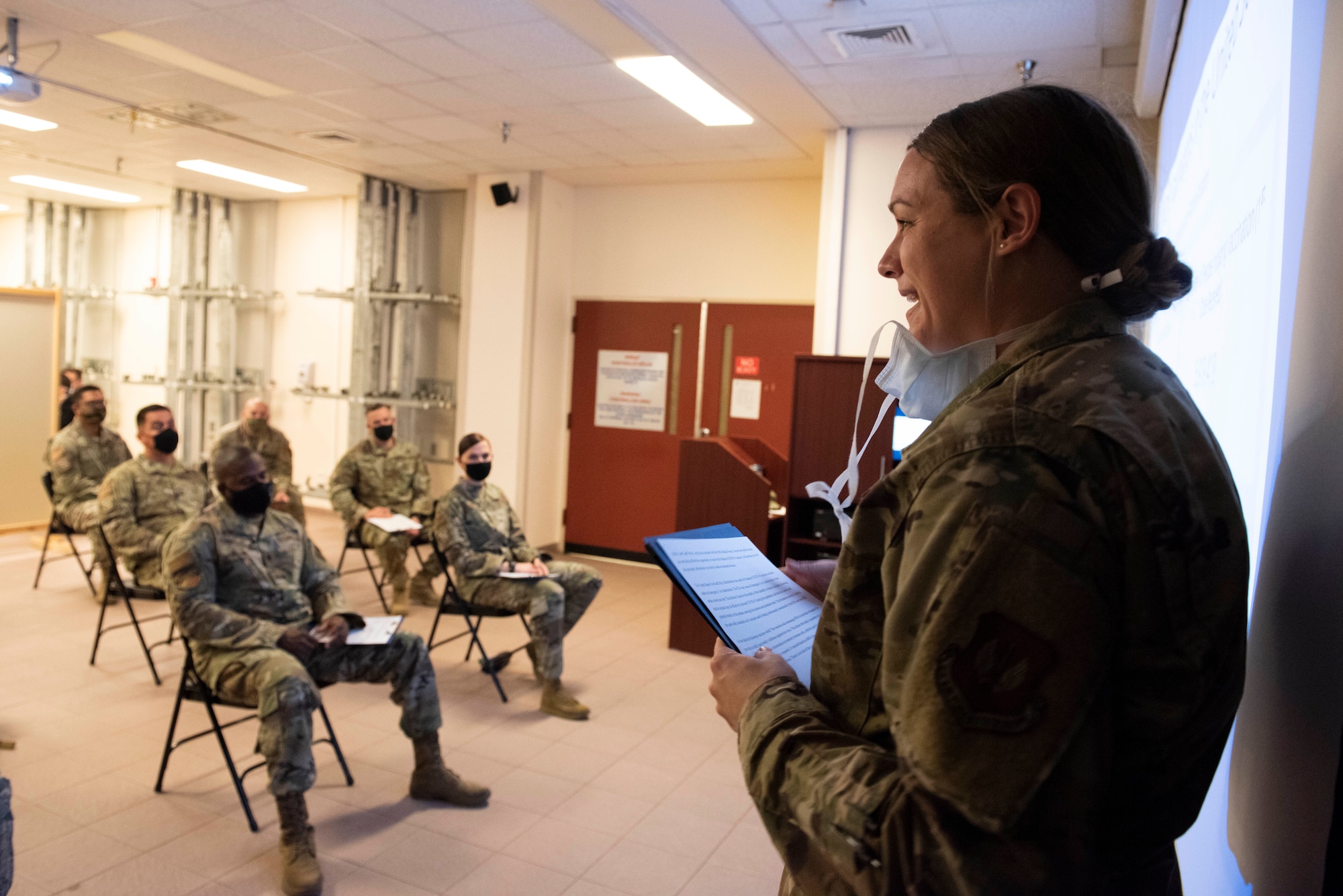 A female captain talks to a small crowd of people in a clinic waiting room.