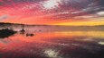 Photo of a beautiful sunrise over a lake.  The sky is pink, purple and yellow.