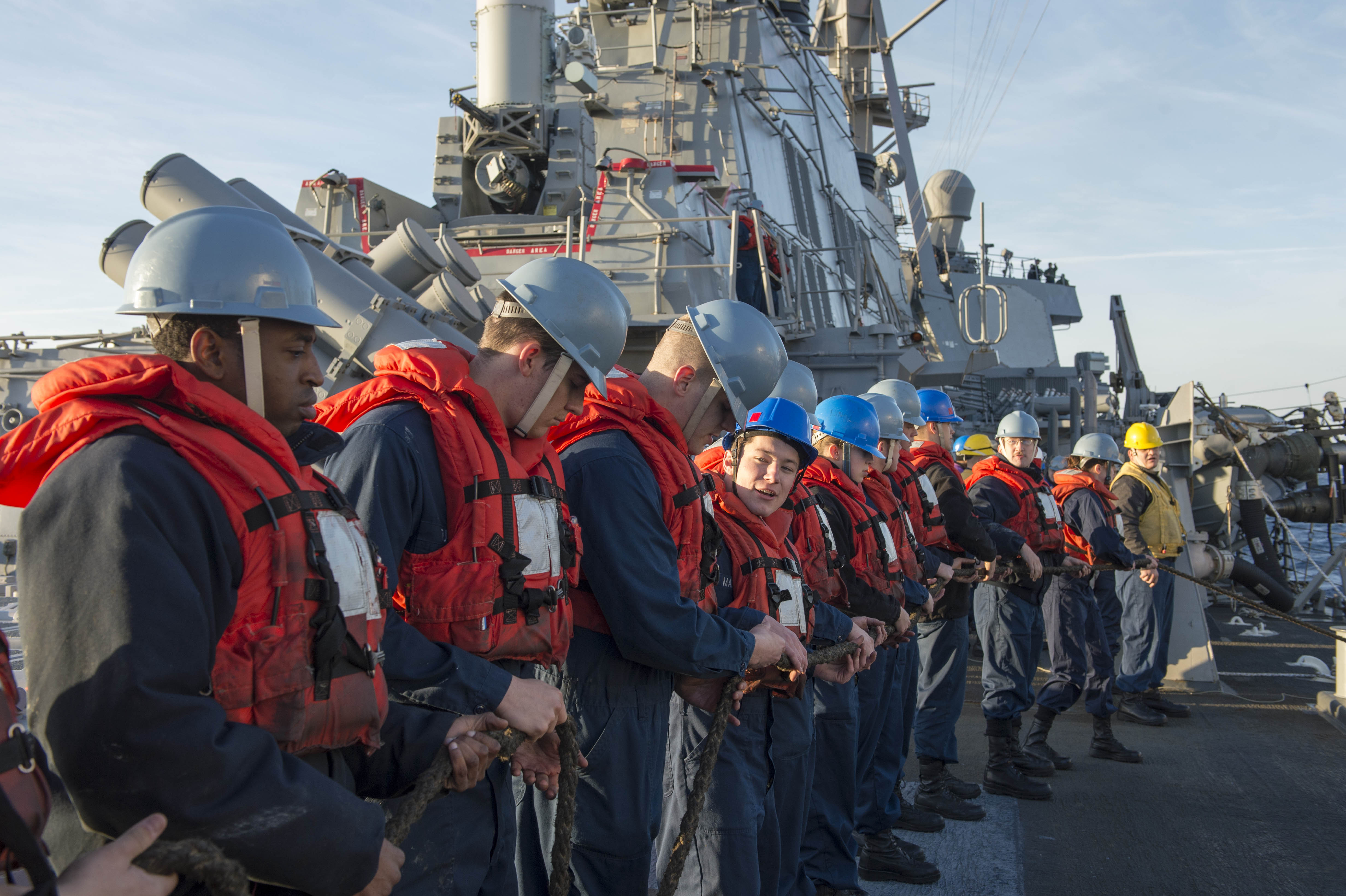 Sailors in life jacket lining up holding the rope on the ship