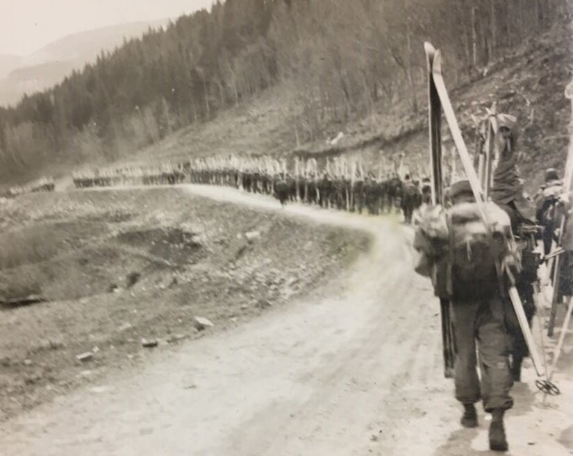 Soldiers march on a road carrying skis