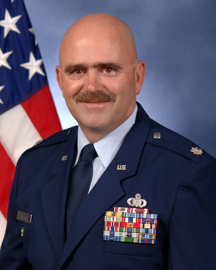 Mark Aicher in military uniform with a blue background and an American flag