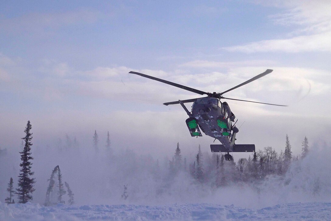 A helicopter prepares to land in the snow; trees seen in the background.