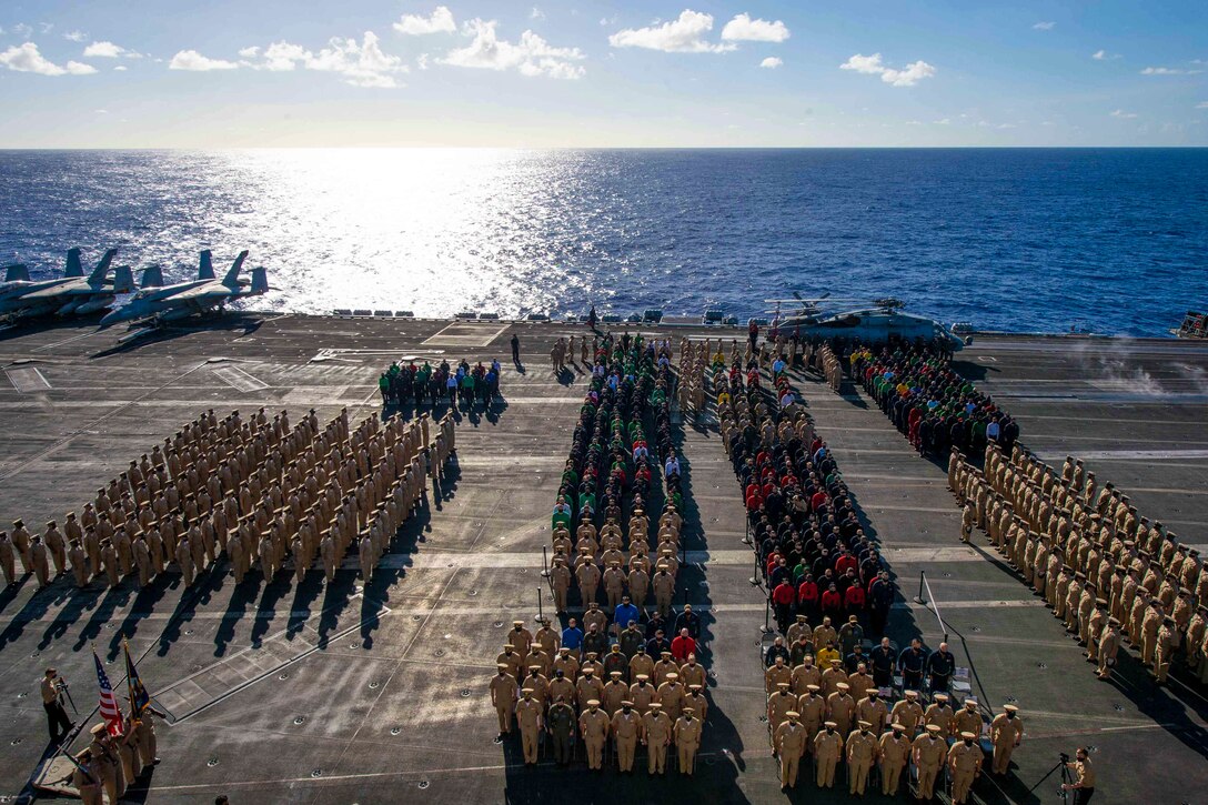 A large group of sailors stand in formation on the deck of a ship.