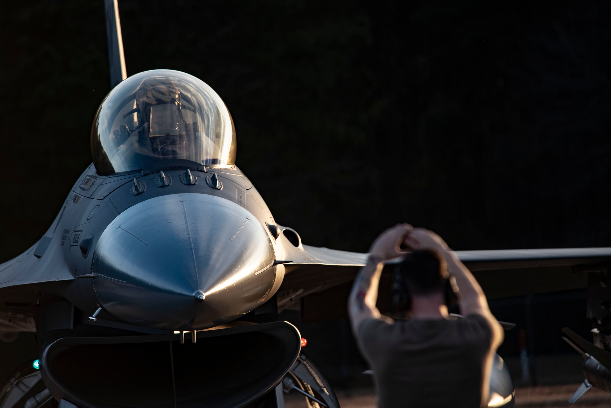 Image of an Airman using hand signals in front of an F-16 Viper.