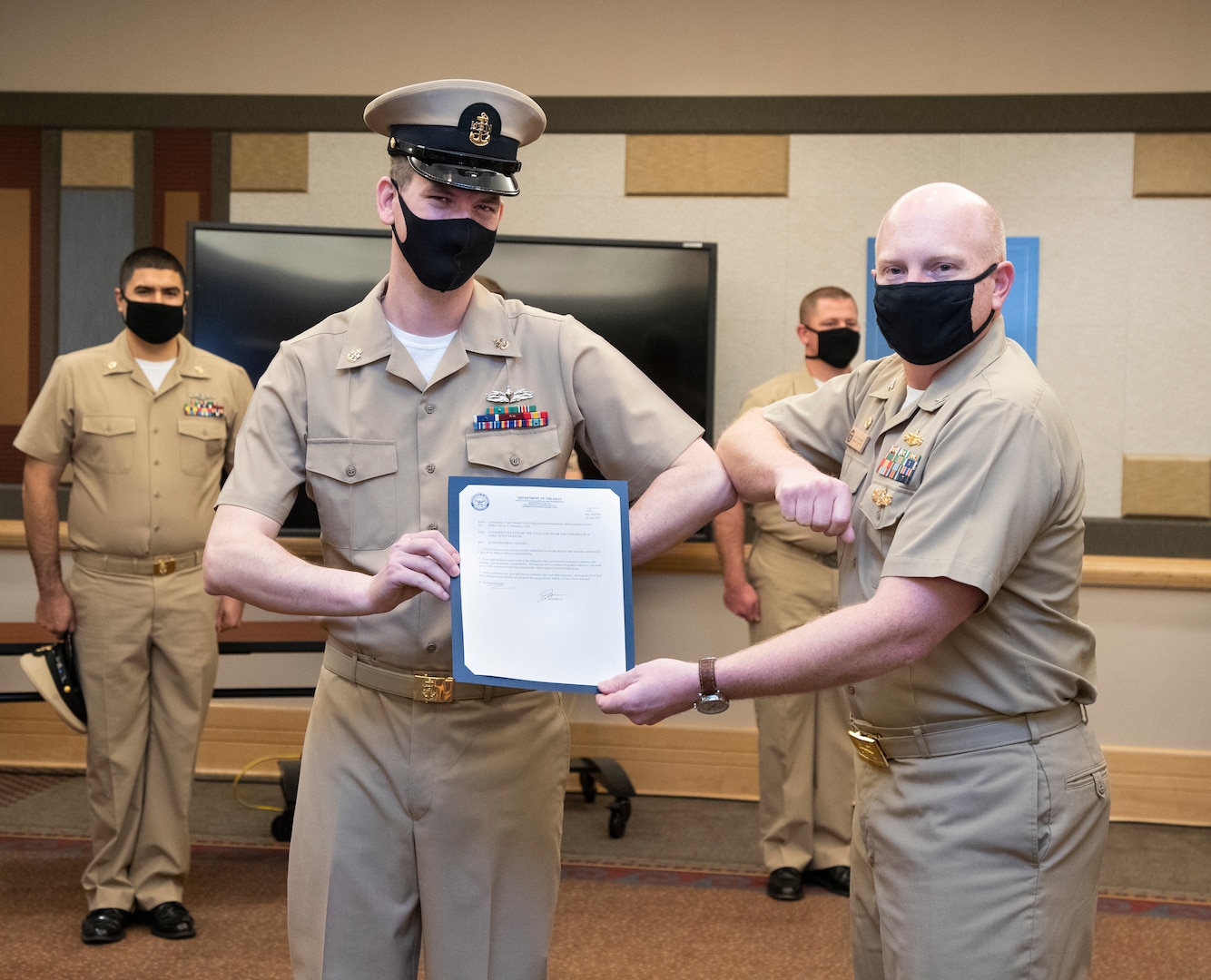 Capt. Jip Mosman, commander, Puget Sound Naval Shipyard & Intermediate Maintenance Facility, presents newly-pinned Chief Petty Officer Devin Donohue with his promotion orders during a during a ceremony Jan. 29, 2021, at Olympic Lodge on Naval Base Kitsap-Bremerton, Washington. The ceremony had limited attendees, with participants and attendees socially distanced to adhere to COVID-19 protective protocols.
