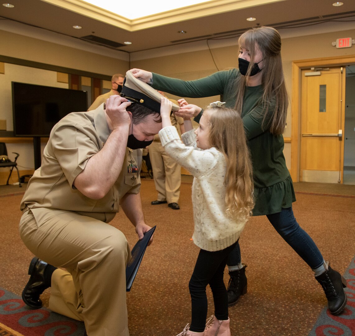 Chief Petty Officer select Austin Rhodes has his chief petty officer anchor insignia pinned onto his uniform by his wife Sarah and daughter Kelby, during a ceremony Jan. 29, 2021, at Olympic Lodge on Naval Base Kitsap-Bremerton, Washington. The ceremony had limited attendees, with participants and attendees socially distanced to adhere to COVID-19 protective protocols.