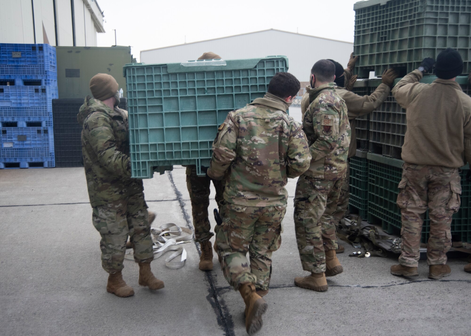 A group of Airmen lifts a large green bin, known as the Titan Tub Bin ll.