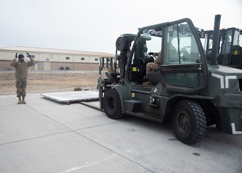 An Airman directs another Airmen who is driving a forklift.