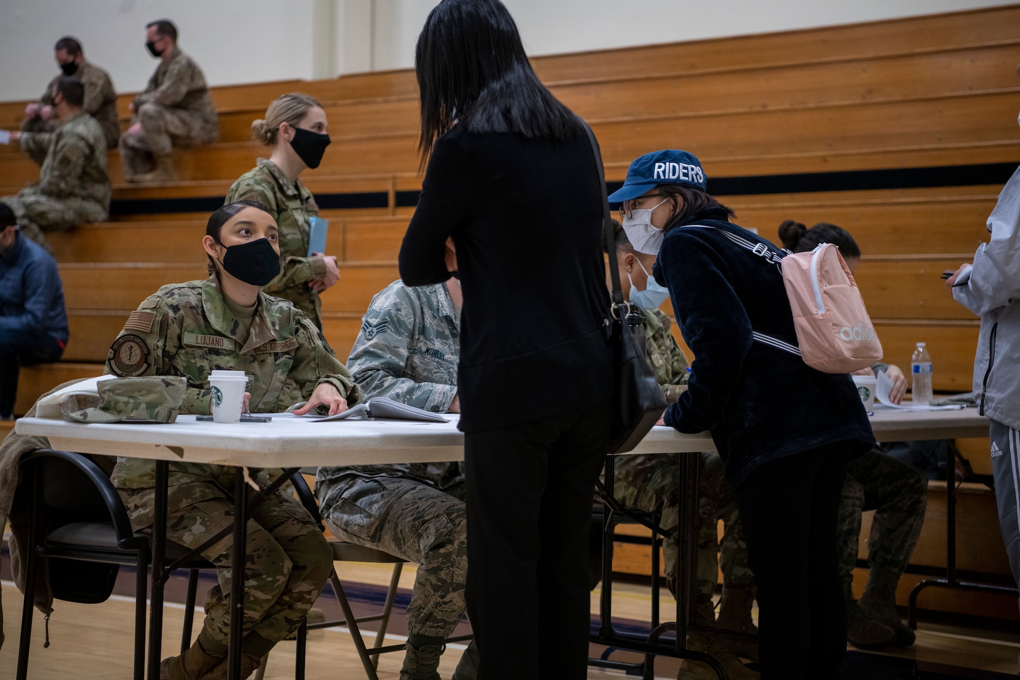 A woman is looking up at another woman while she is sitting behind a table and the woman on the other side of the table is looking at her.