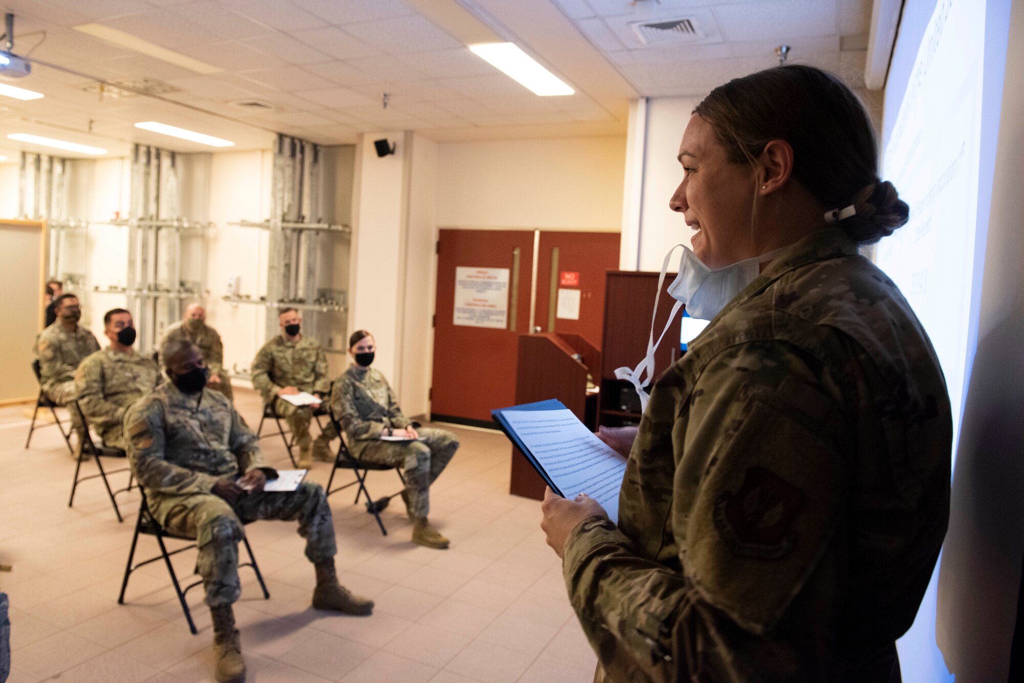 A female captain talks to a small crowd of people in a clinic waiting room.