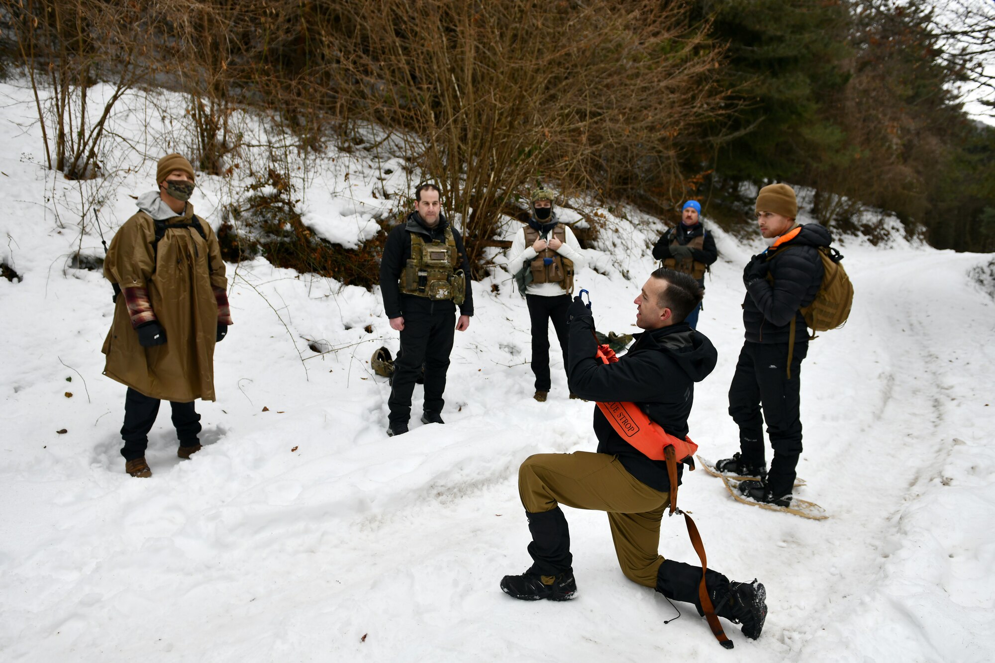 U.S. Air Force Tech. Sgt. Mike Rutland, 31st Operations Support Squadron Survival, Evasion, Resistance and Escape (SERE) noncommissioned officer in charge, kneeling, demonstrates how to use a rescue strop when hoisted by a helicopter during combat survival training in the mountains near Pian Cansiglio, Italy, Jan. 21, 2021. While also teaching Airmen the skills needed to survive in a contested environment, the training brought together SERE and search and rescue personnel from the U.S. and Italian air forces. (U.S. Air Force photo by Staff Sgt. K. Tucker Owen