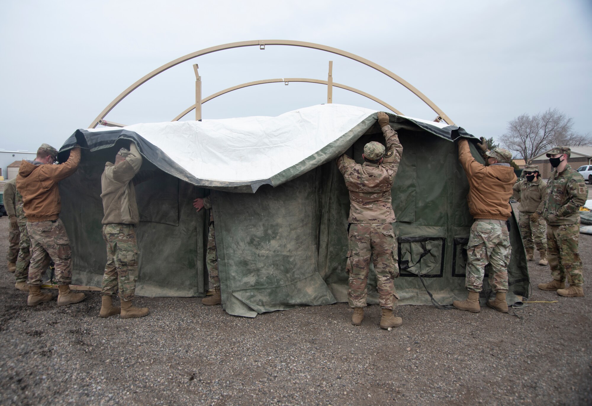A group of Airmen lifts a door frame of a small shelter system tent.