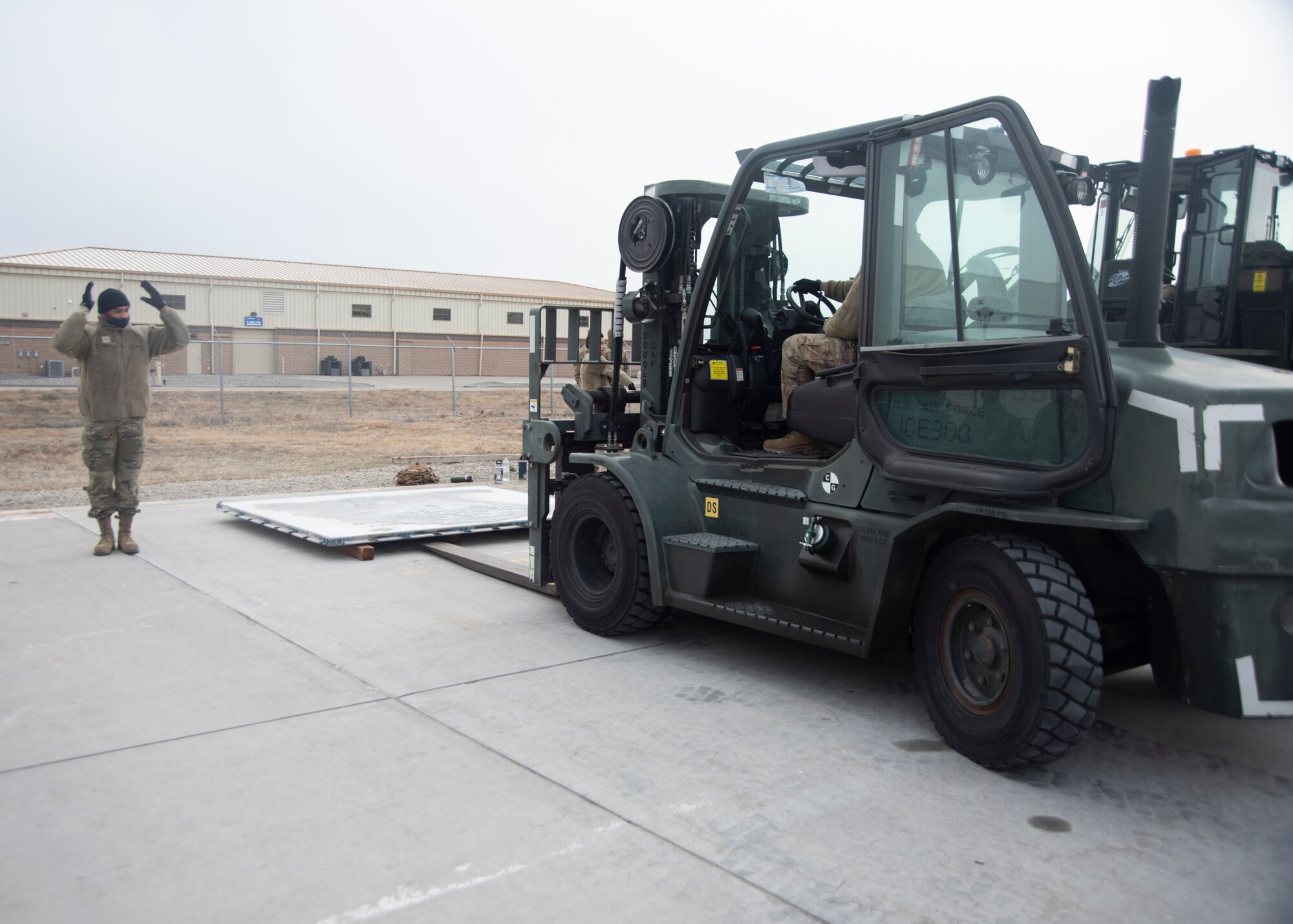 An Airman directs another Airmen who is driving a forklift.