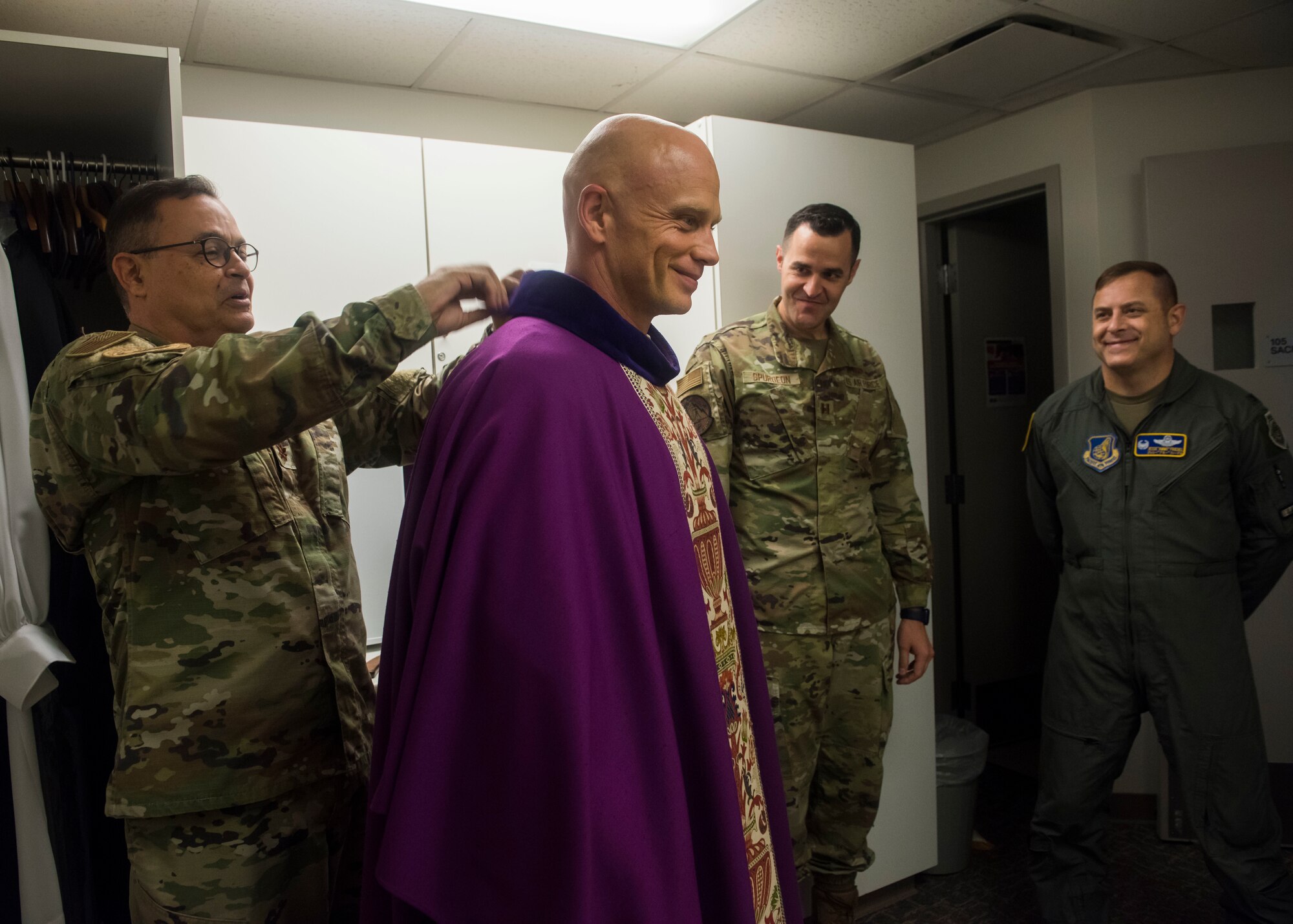 Military members help place religious robes onto each other.