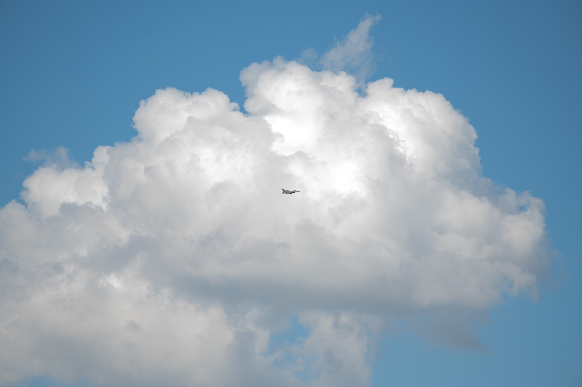 A fighter jet soars through fluffy white clouds.