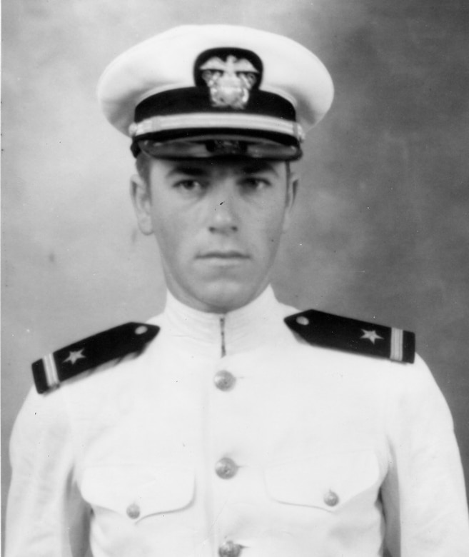 A young sailor in his white dress uniform and cap looks forward.