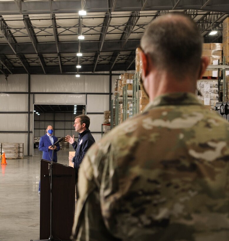 Kentucky Army National Guard 1st Sgt. Dylan Molohon listens as Governor Andy Beshear speaks during a press conference held at the supply warehouse in Frankfort, Ky., Sept. 10, 2020.