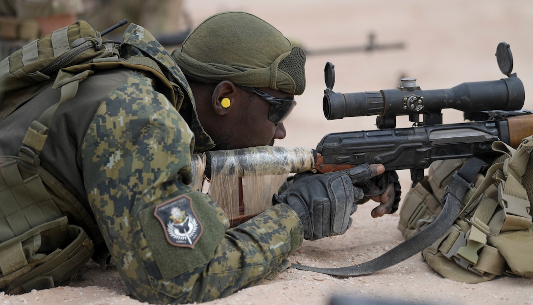 A soldier lays on the ground and aims a rifle.