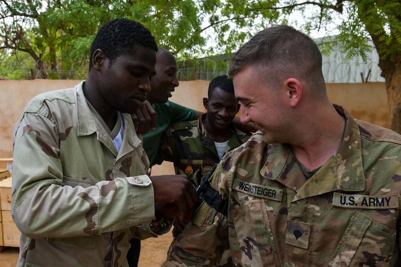 A soldier adjusts gear on the arm of another soldier.