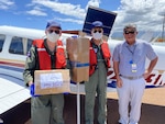 A Coast Guard Auxiliary aircrew (left) stands with Brian Kamimoto (right), assistant airport superintendent Maui District at the Maui Airport Fire Station while picking up response supplies for delivery from Maui to Lanai, March 28, 2020. The pilots transported COVID-19 supplies, including temperature reading thermometers and hand sanitation equipment, from the Maui Airport Fire Station to personnel at Lanai Airport for use by airport staff. (U.S. Coast Guard photo by Berry Redmayne/Released)