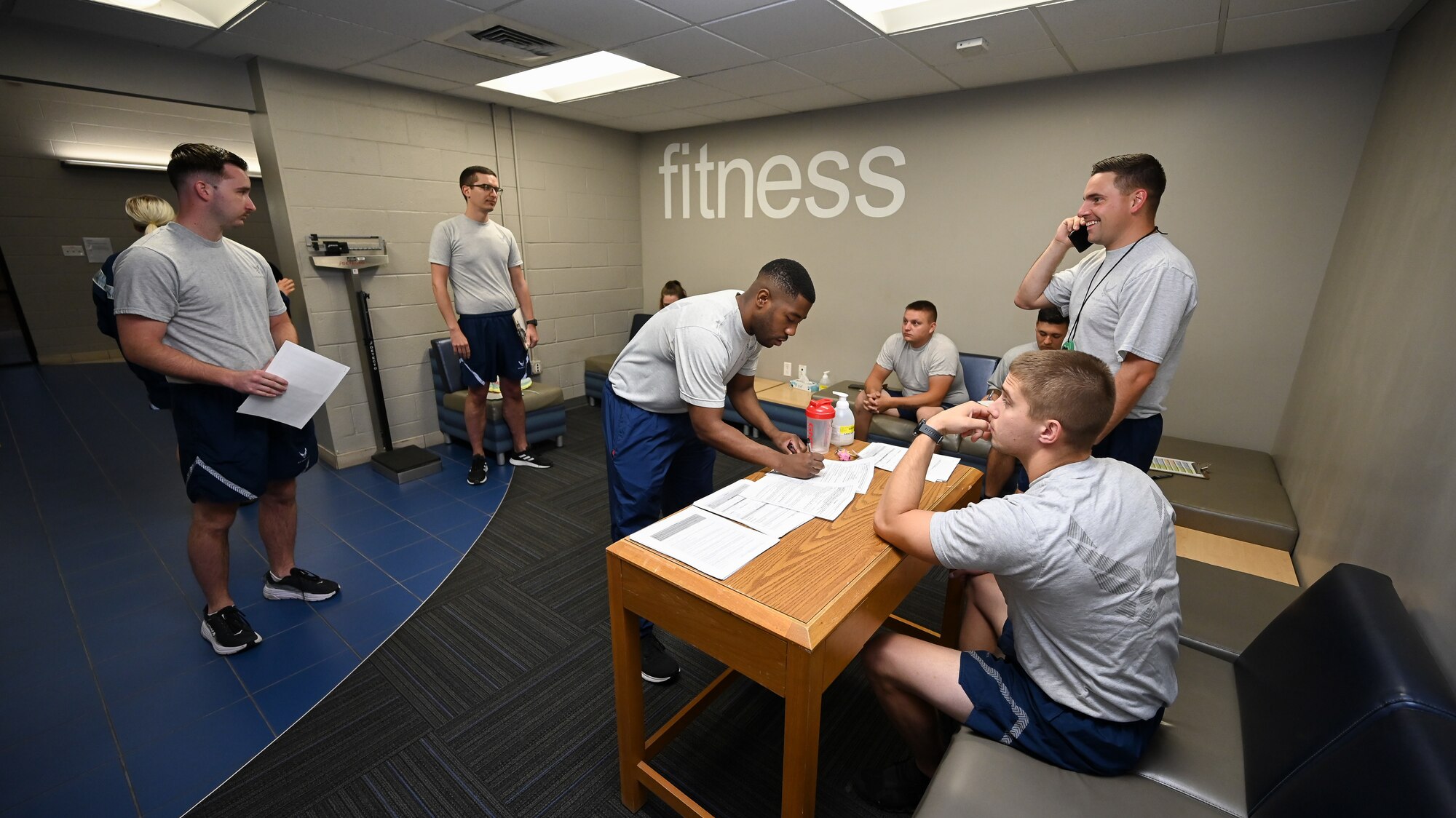 Tech. Sgt. Keedrick Mitchell signs in to take a physical fitness test in the fitness center lobby while Airmen around him mingle.