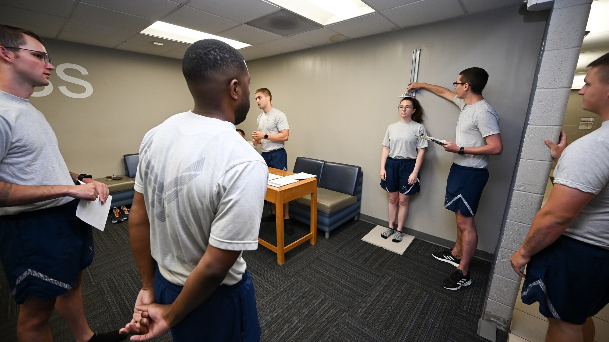 Airman 1st Class Savannah Miller has her height recorded inside a training room while other Airmen watch in the foreground.