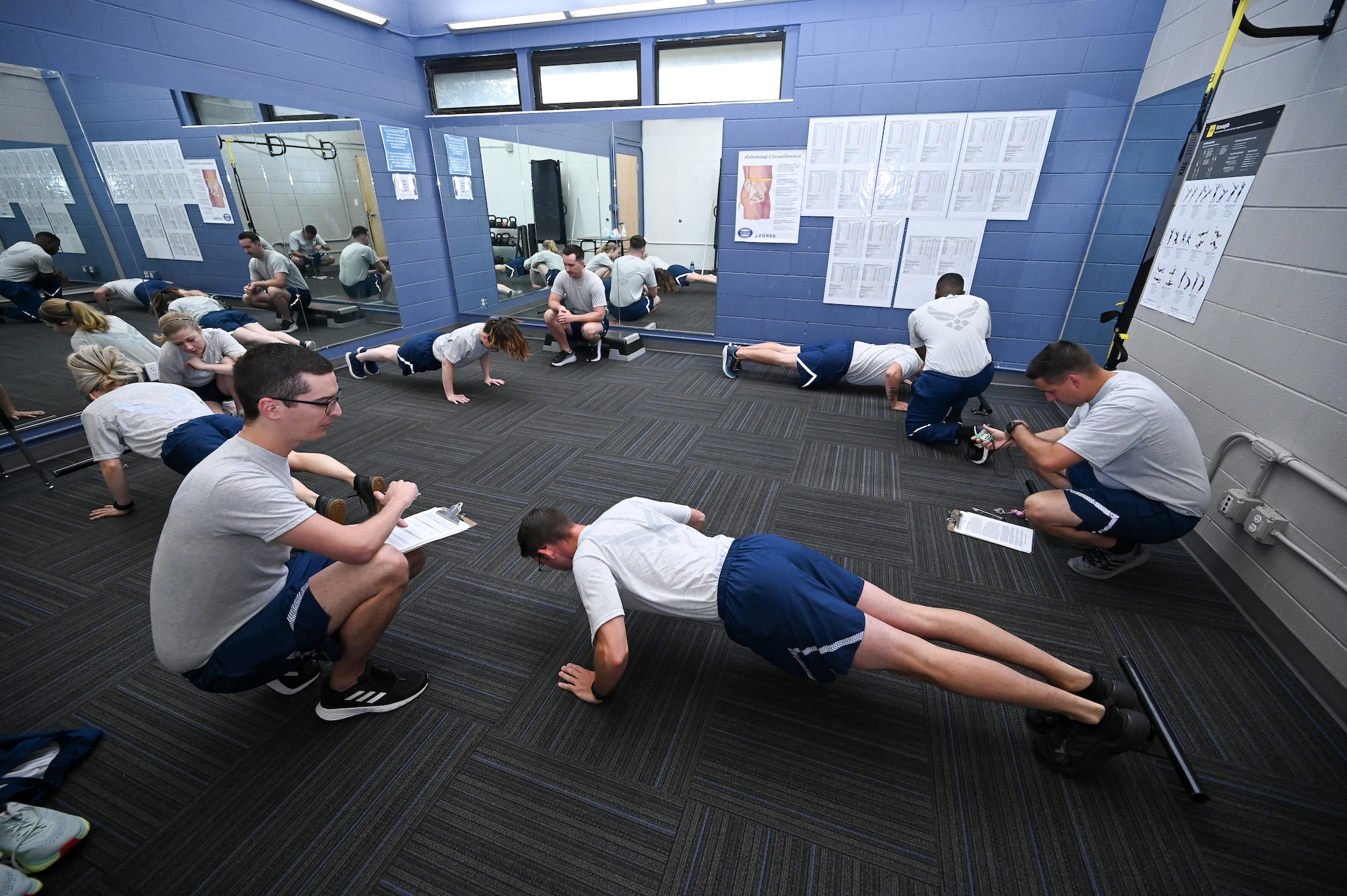 Airmen do push-ups during a fitness assessment test inside a training room.