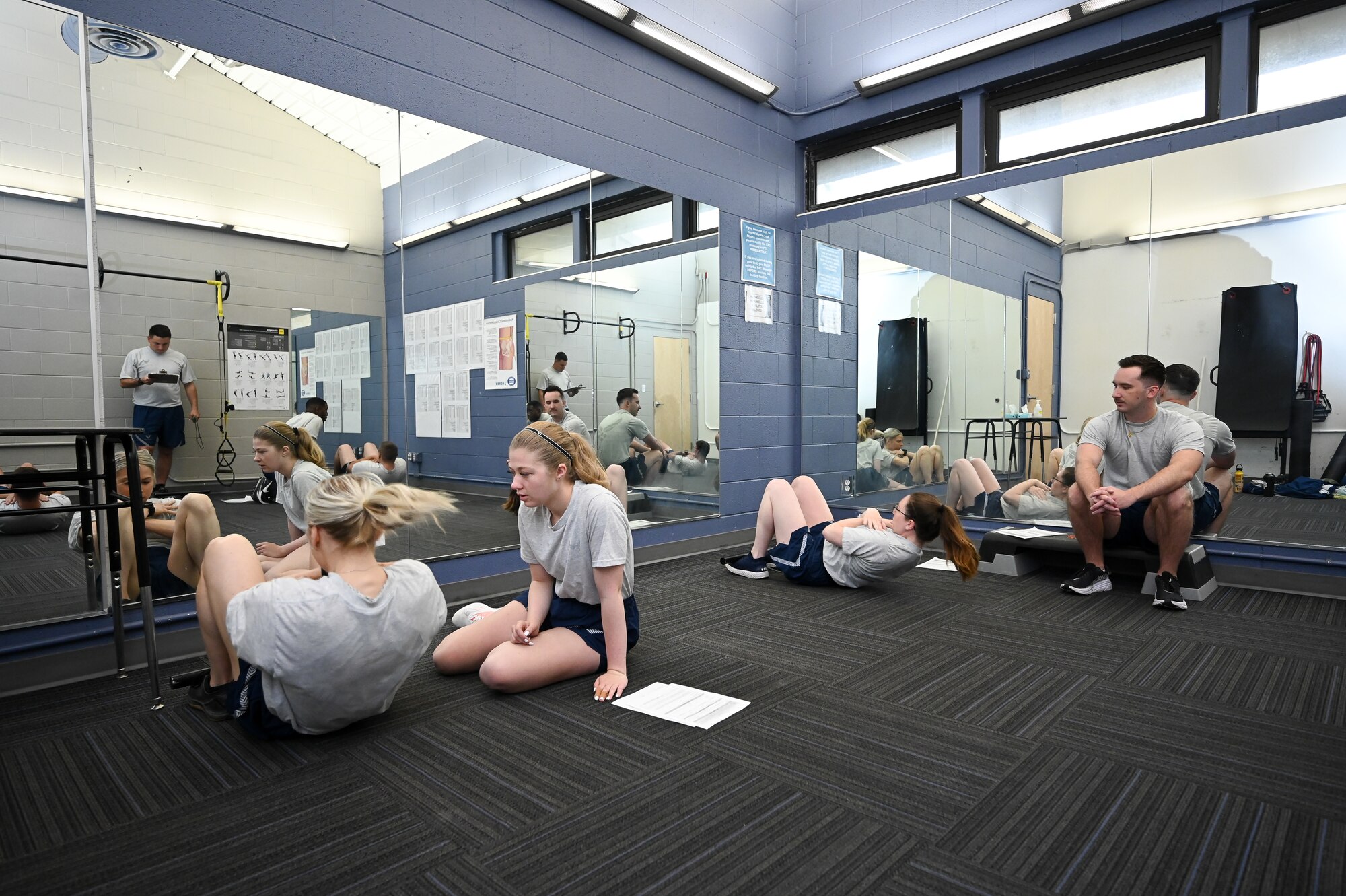 Airmen do sit-ups during a fitness assessment inside a training room.