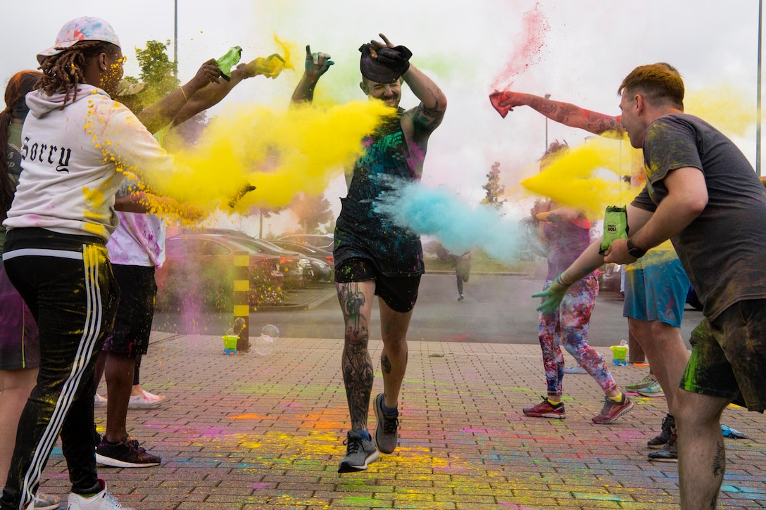 An airman runs through a crowd as others throw colorful powder.