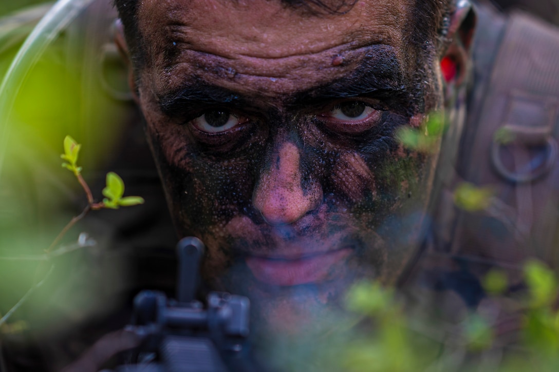 A soldier in camouflage is seen close up while holding a weapon.