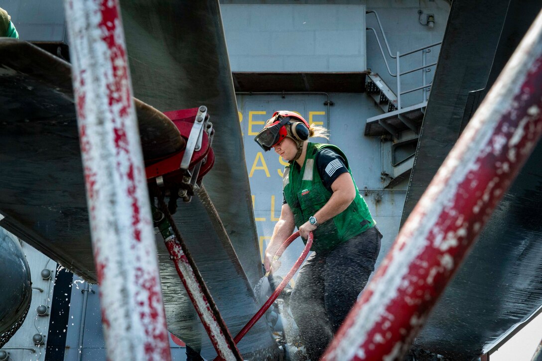 A sailor uses a hose to wash a helicopter.