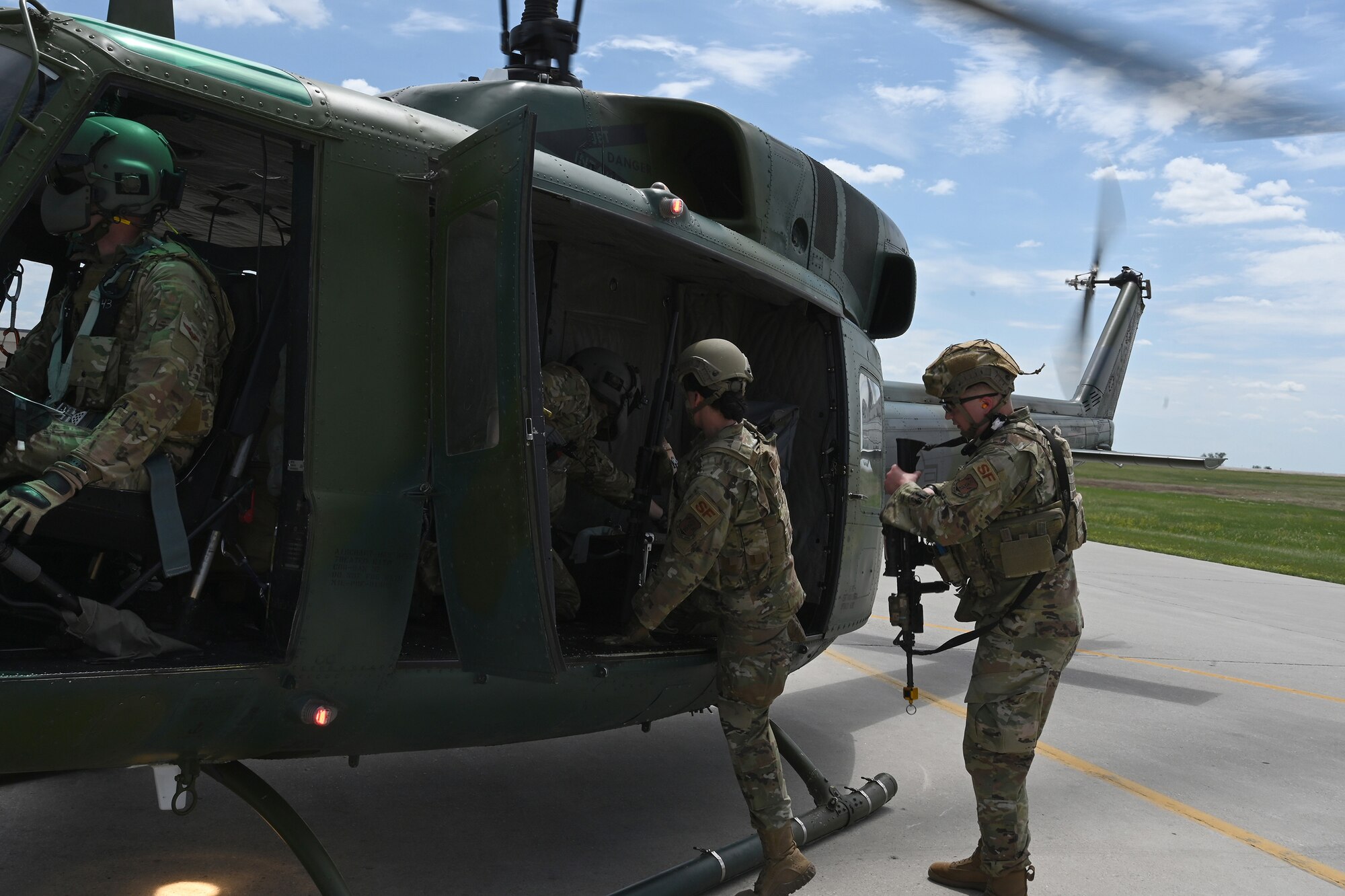 Two North Dakota Air National Guard 219th Security Forces Squadron members in uniform climb into the open door of a UH-1N Huey helicopter as it prepares for launch at the Minot Air Force Base, N.D., June 24, 2021.