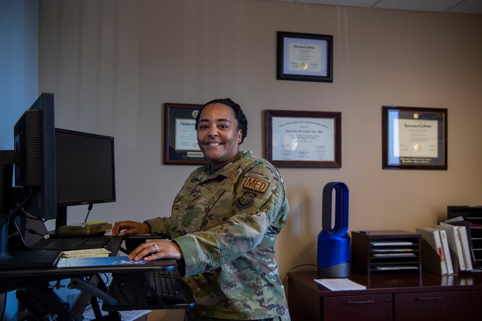 An airman poses for a photo by her computer in an office.