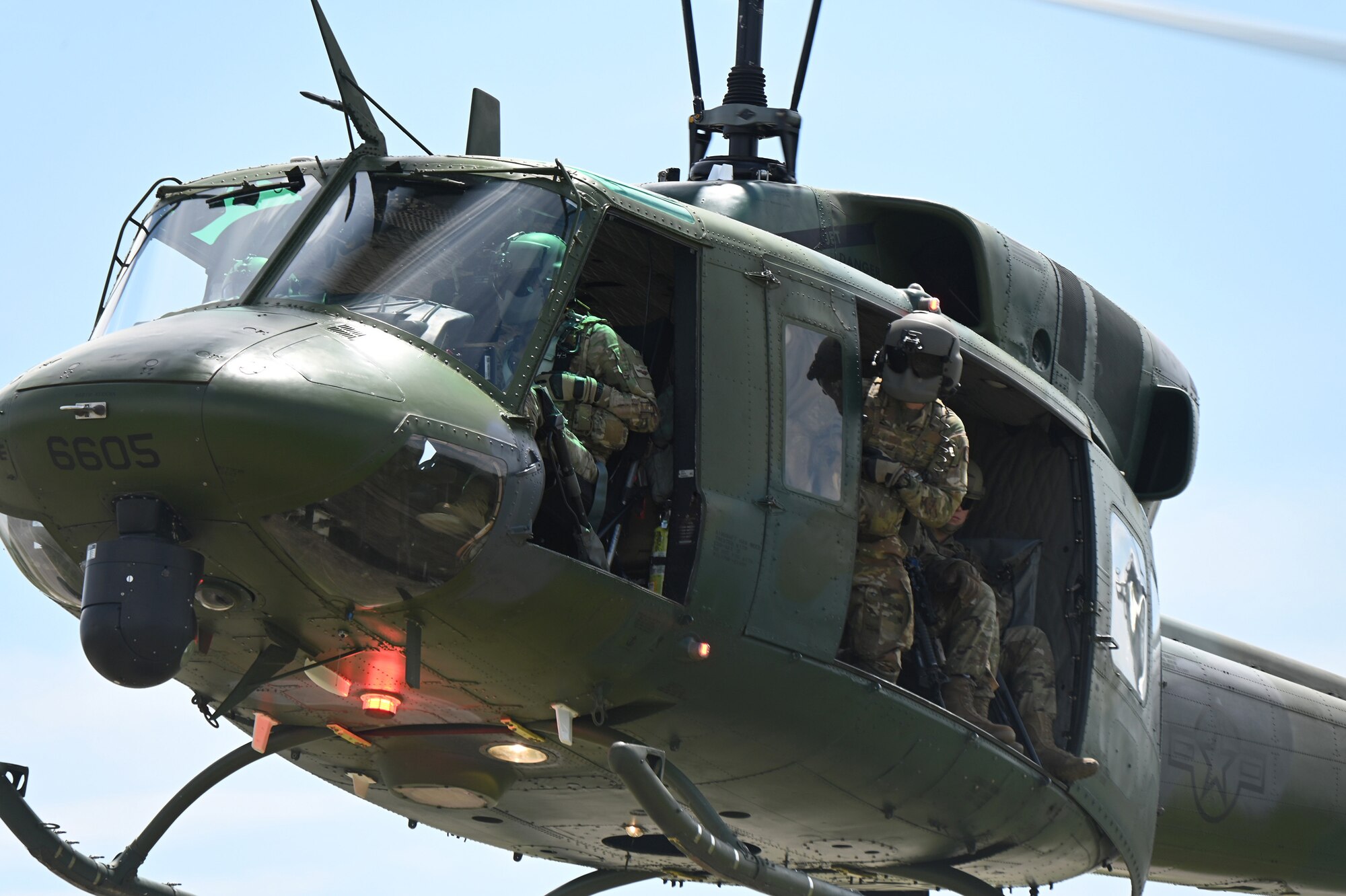 A three-person crew of a 54th Helicopter Squadron operate a UH-1N Huey helicopter as the flight engineer peers out an open door while watching the ground for landing during a training exercise at the Minot Air Force Base, N.D., June 24, 2021.