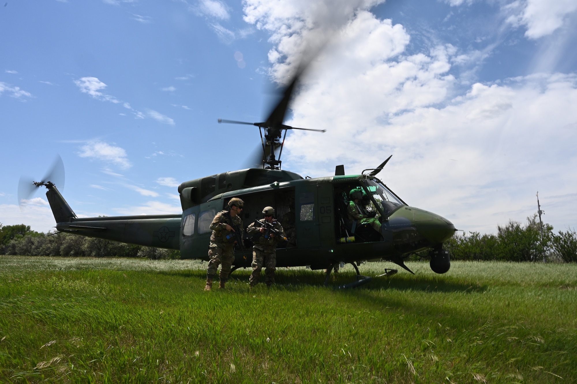 Two members of the 219th Security Forces Squadron in military uniform hop off a UH-1N Huey helicopter with rotor blades in motion during a training exercise at the Minot Air Force Base, N.D., June 24, 2021.