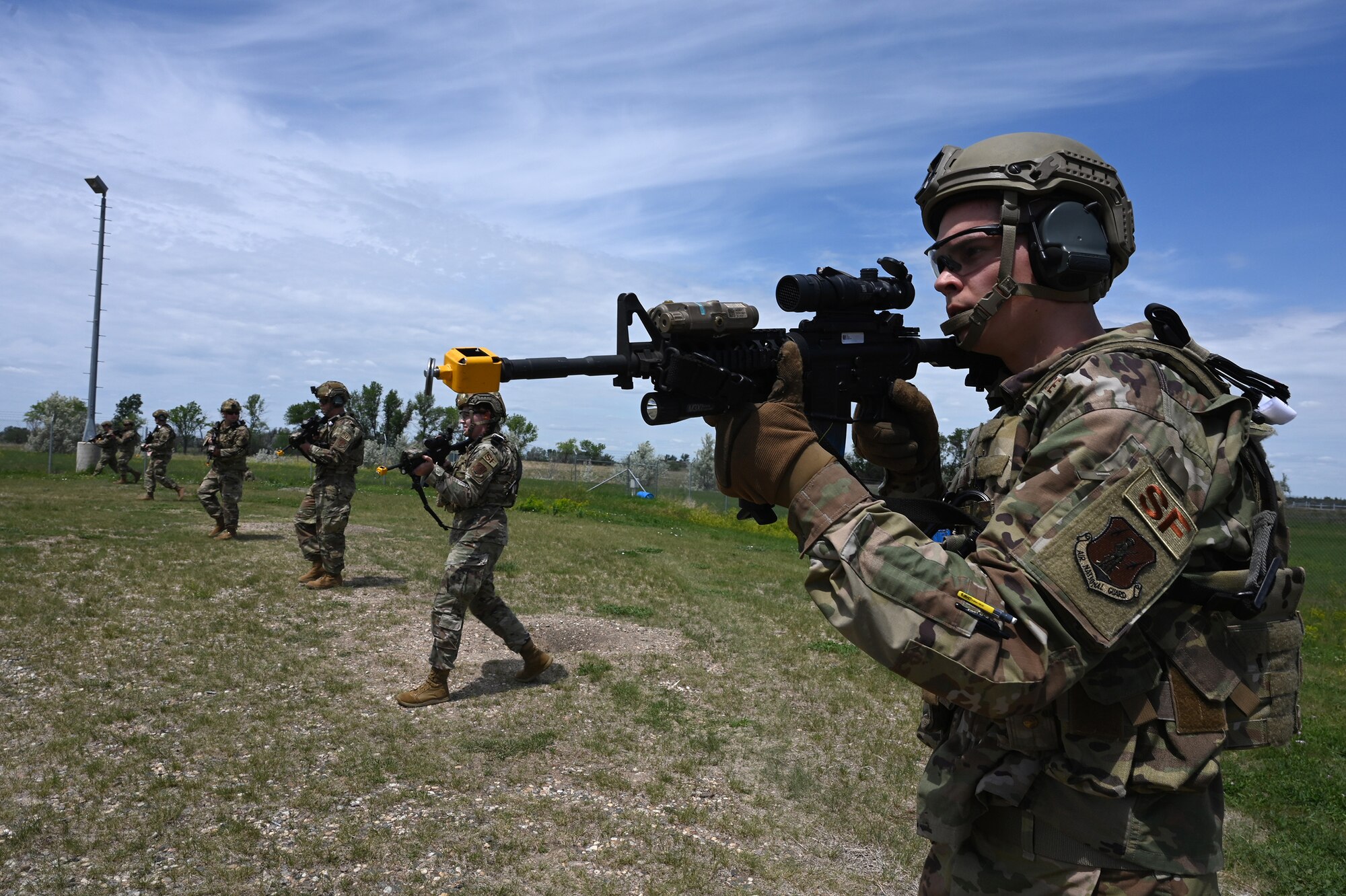 Seven members of the 219th Security Forces Squadron 219th Security Forces Squadron walk spread out in a line as they point M4 rifles ahead of them during a training exercise on a training missile launch facility at the Minot Air Force Base, N.D., June 24, 2021.