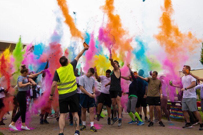 A group of people wearing fitness attire crowd together and throw different colored powders into the air.