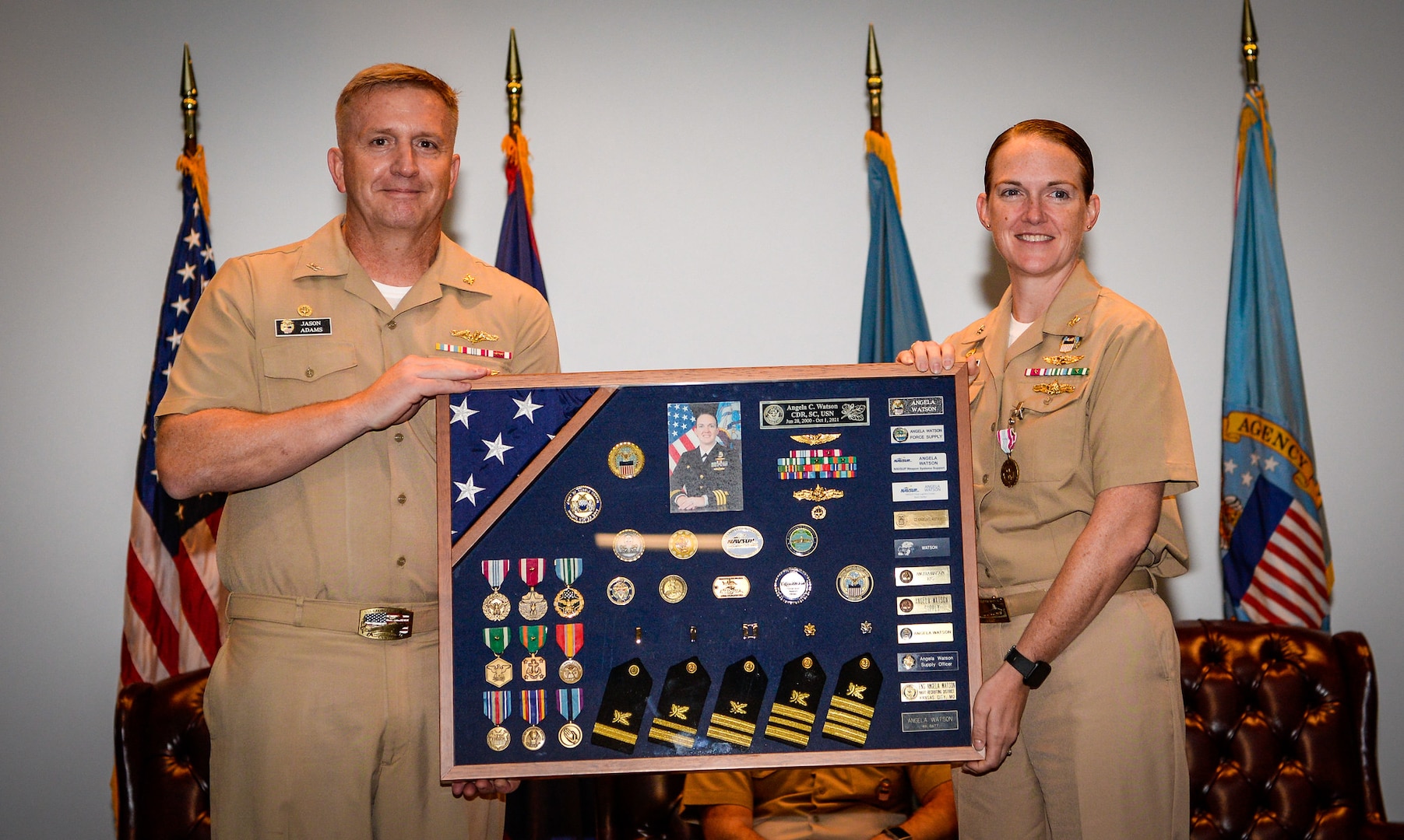 Two people in Navy khaki uniforms hold a large military shadow box