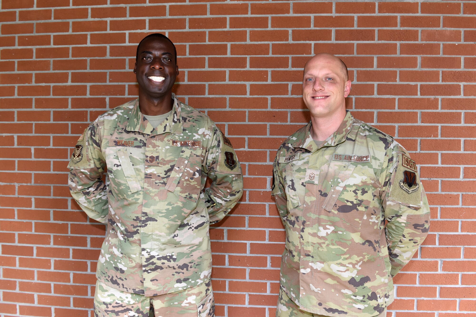 Photo shows two Airmen standing in front of brick wall.