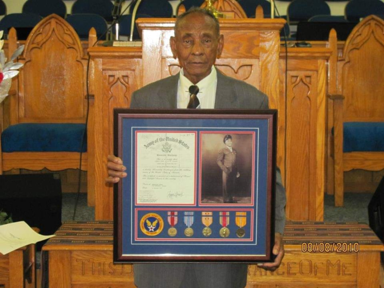 An older man standing in front of a lectern  holds a plaque.