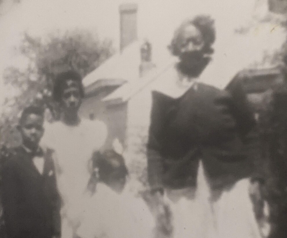 A boy, two girls and a woman pose for a photo in front of a house.