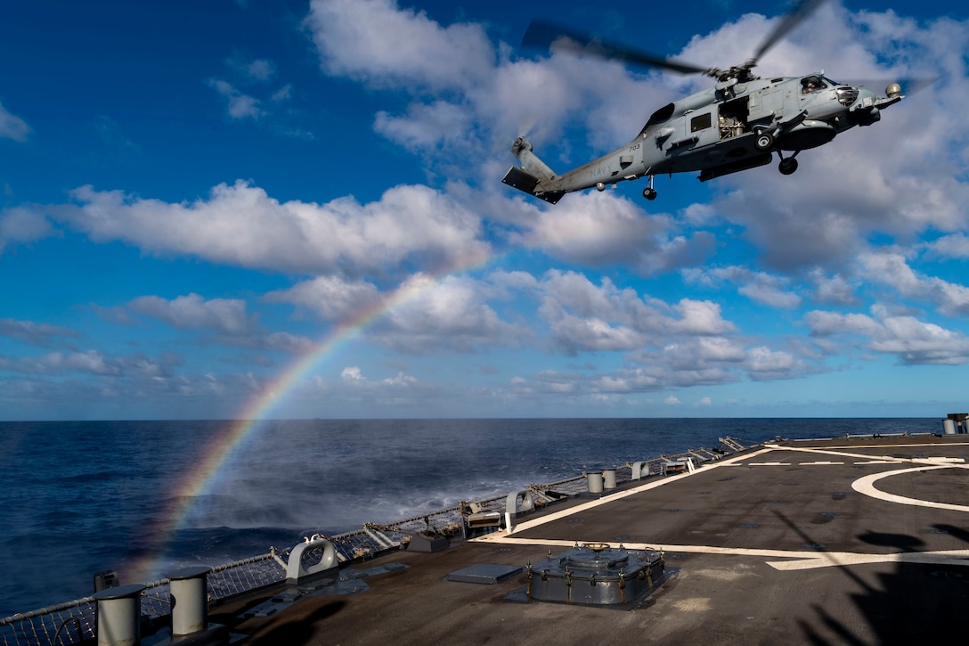 A helicopter takes off from a ship in the ocean  as a rainbow appears behind it.