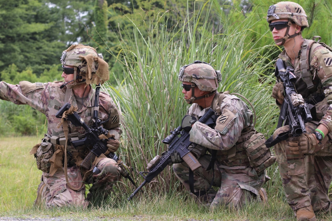 Three soldiers kneel together in a field.