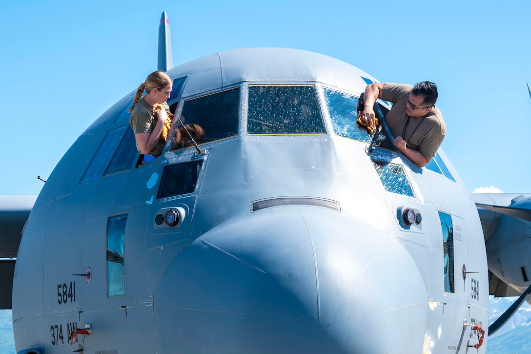Two airmen clean the windows of a large aircraft.