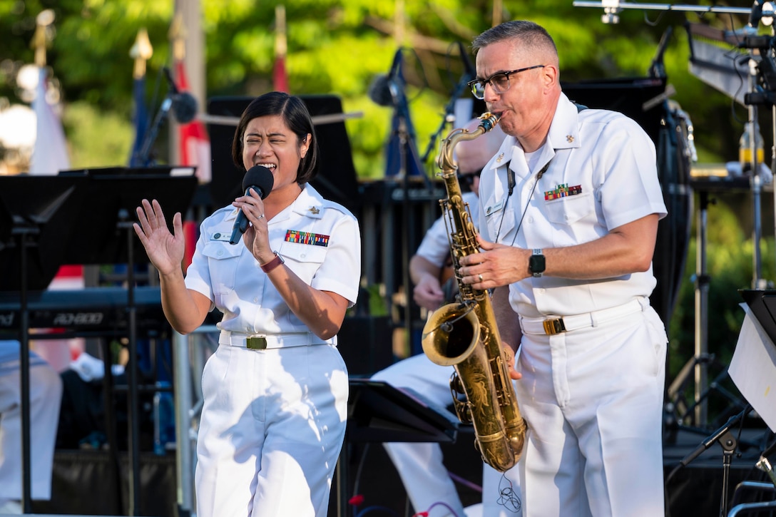 A sailor sings into a microphone as another sailor plays a saxophone.
