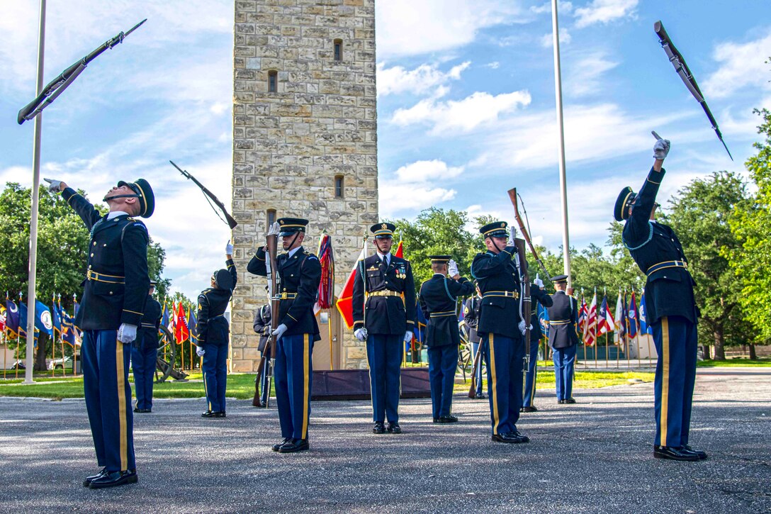 Soldiers stand in formation as some twirl rifles in the air.