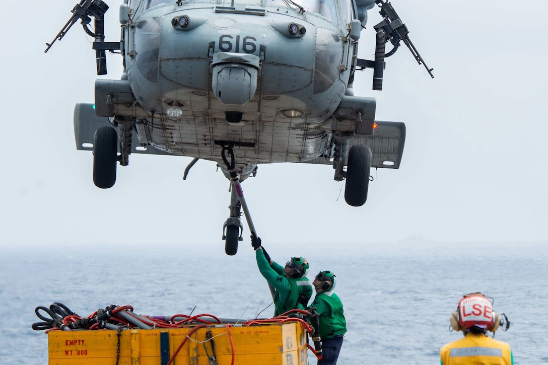 Sailors attach cargo to a helicopter on a ship at sea.