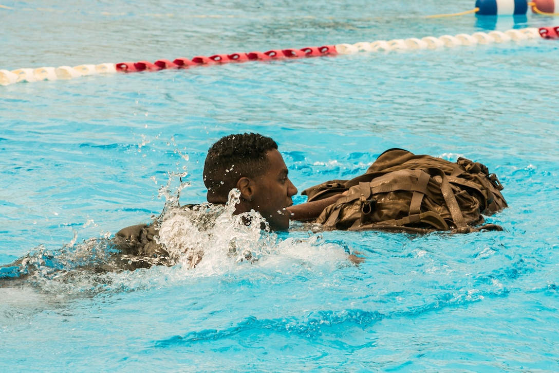 A Marine swims with a backpack in a pool.