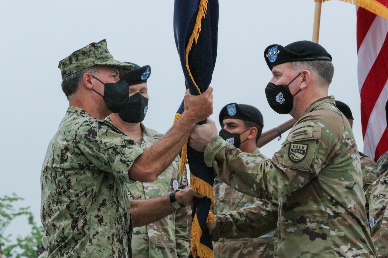 Two service members hold a flag in between their hands.