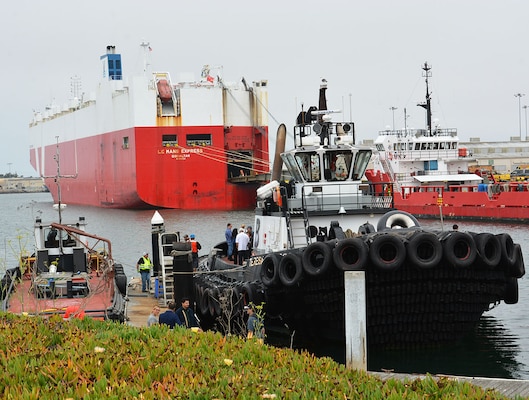 City and port officials with the Port of Hueneme, along with representatives with the U.S. Army Corps of Engineers Los Angeles District, begin loading onto a tugboat in the Port of Hueneme – in the shadow of a large cargo vessel – to take a tour of the harbor following a ribbon-cutting ceremony celebrating the completion of the deepening of Port Hueneme Harbor June 28 at Port Hueneme, California.